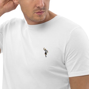 May include: A white t-shirt with a small black and white illustration of a referee signaling a goal.