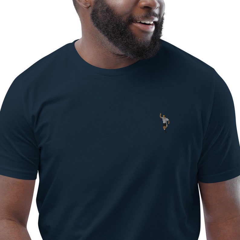 May include: A navy blue t-shirt with a small embroidered image of a referee signaling a touchdown.