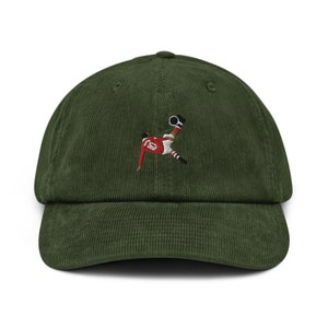 May include: A green corduroy baseball cap with an embroidered image of a soccer player kicking a ball.