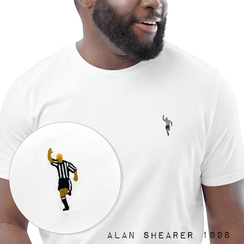 May include: White t-shirt with a black and white embroidered image of a soccer player celebrating a goal. The text "ALAN SHEARER 1 998" is printed below the image.