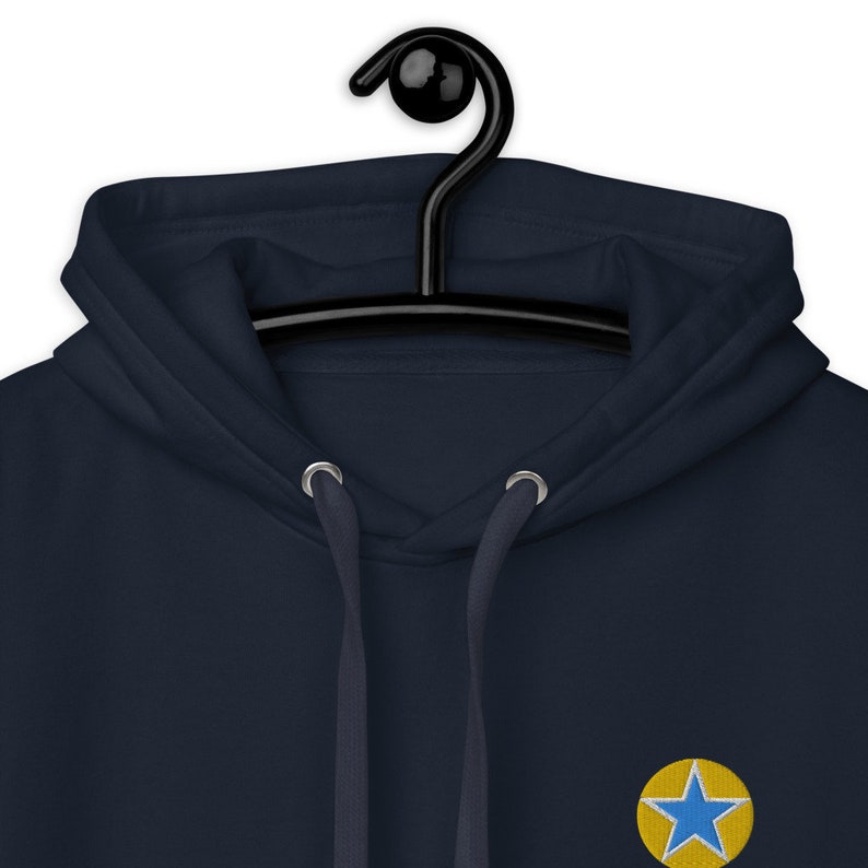 K&ouml;nnte beinhalten: Ein marineblauer Kapuzenpullover mit einem gestickten gelben und blauen Stern auf der Vorderseite.