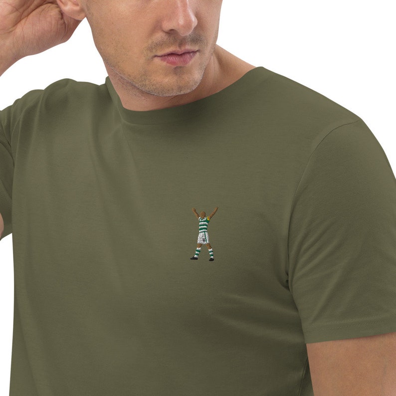 May include: A green t-shirt with an embroidered image of a soccer player celebrating a goal.