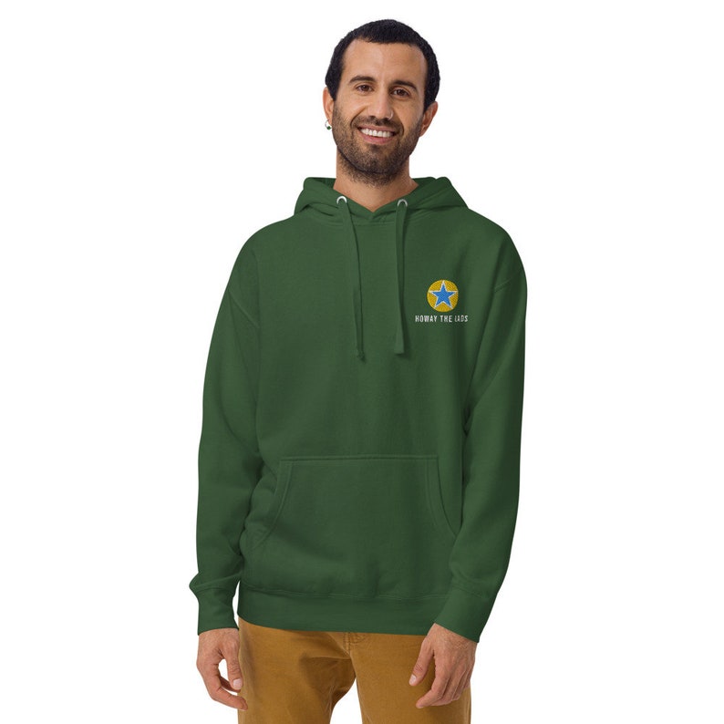 K&ouml;nnte beinhalten: Ein dunkelgr&uuml;ner Kapuzenpullover mit einem gelben Kreis und einem blauen Stern-Motiv auf der Vorderseite. Der Text "HOKAY THE LADS" ist unter dem Motiv aufgedruckt.