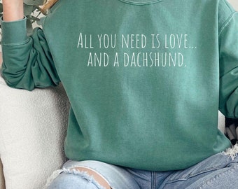 May include: A light green sweatshirt with the text "All you need is love... and a dachshund." printed in white.