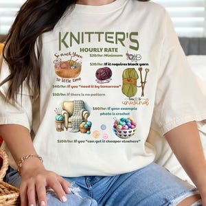 May include: A white t-shirt with a humorous graphic about knitter's hourly rates. The graphic features yarn, knitting needles, and a crochet hook. The text reads "Knitter's Hourly Rate $20/hr: Minimum $30/hr: If it requires black yarn $40/hr: If you "need it by tomorrow" $50/hr: If there is no pattern $80/hr: If your example photo is crochet $100/hr: If you "can get it cheaper elsewhere" Time to unwind"