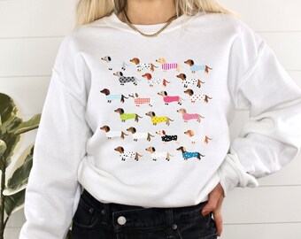 May include: White sweatshirt with a colorful pattern of dachshunds wearing different outfits.