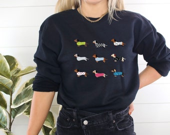 May include: A black sweatshirt with a graphic print of nine dachshunds wearing different patterned pajamas.