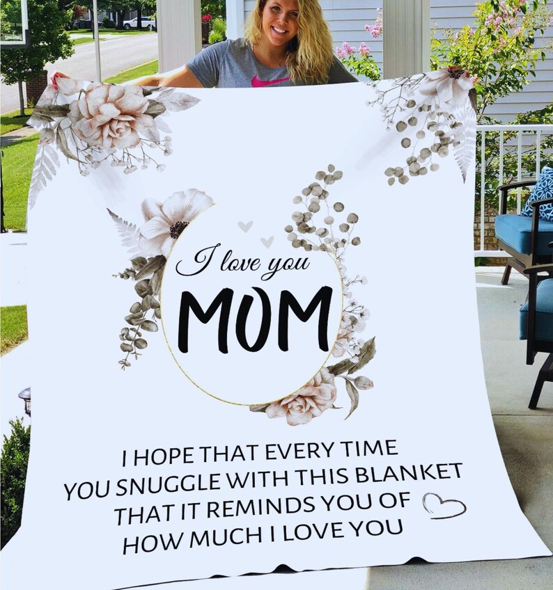 Puede incluir: Una manta blanca con un dise&ntilde;o floral y el texto "I love you MOM". El texto est&aacute; en un c&iacute;rculo dorado con un dise&ntilde;o floral. La manta tambi&eacute;n tiene el texto "I hope that every time you snuggle with this blanket that it reminds you of how much I love you".