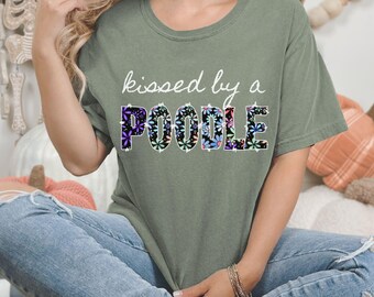 May include: A green t-shirt with the text "kissed by a POODLE" in white lettering. The word "POODLE" is made up of colorful flowers.