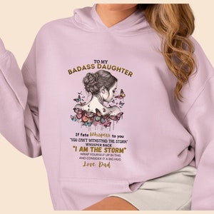 May include: A light purple hoodie with a gold graphic of a woman with butterflies and the text "To My Badass Daughter" and "If fate whispers to you 'You can't withstand the storm' whisper back 'I am the storm' Wrap yourself up in this and consider it a big hug Love. Dad"
