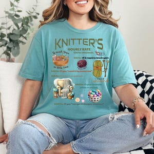 May include: A teal blue t-shirt with a humorous graphic about knitter's hourly rates. The graphic includes yarn, needles, and a chair. The text reads "KNITTER'S HOURLY RATE $20/hr Minimum $30/hr if it requires black yarn $50/hr if you "need it by tomorrow" $100/hr if you can knit it the cheapest and fastest"