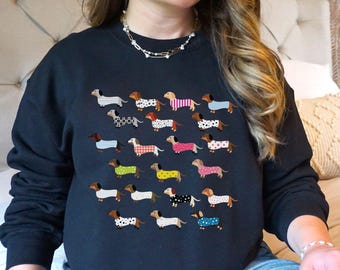 May include: A black sweatshirt with a pattern of colorful dachshunds. The dachshunds are all different colors and patterns, and they are arranged in a grid pattern on the front of the sweatshirt.