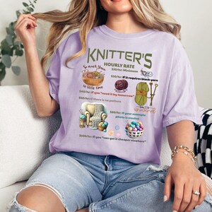 May include: A purple t-shirt with a humorous graphic that reads "Knitter's Hourly Rate" and lists different prices for knitting projects based on factors like yarn color, time constraints, and complexity. The graphic includes illustrations of yarn, knitting needles, and a crocheted item.