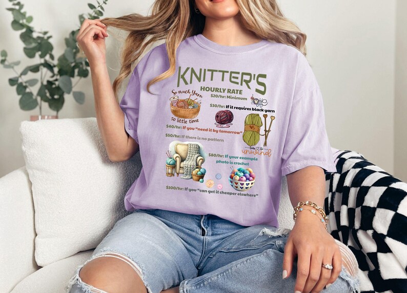 May include: A purple t-shirt with a humorous graphic that reads "Knitter's Hourly Rate" and lists different prices for knitting projects based on factors like yarn color, time constraints, and complexity. The graphic includes illustrations of yarn, knitting needles, and a crocheted item.