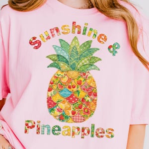 Puede incluir: Camiseta rosa con un diseño de piña de patchwork colorido y las palabras "Sunshine & Pineapples". La piña está hecha de varias telas estampadas, creando una estética vibrante y alegre. Es una prenda de vestir informal.