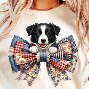 May include: A cream-colored t-shirt featuring a graphic of a black and white puppy peeking out from behind a large, multi-textured bow. The bow is composed of various fabric patterns, including red and white gingham, blue denim, and floral prints.