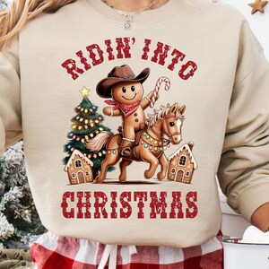 This set includes 2 high-quality PNG designs featuring a smiling gingerbread man dressed as a cowboy, riding a festive horse decorated with Christmas lights, surrounded by gingerbread houses and a glowing tree. One design displays the gingerbread man and horse only with no distressing. The second PNG has the text “Ridin’ Into Christmas” in red with a transparent distressing throughout the design.