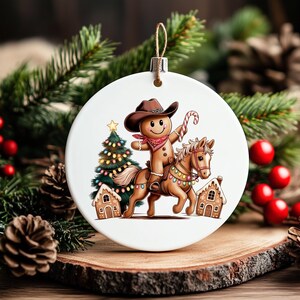 K&ouml;nnte beinhalten: Ein rundes, wei&szlig;es Keramikornament mit einem Lebkuchenmann, der einen braunen Cowboyhut und ein rotes Halstuch tr&auml;gt und auf einem braunen Pferd reitet. Das Motiv zeigt zudem einen geschm&uuml;ckten Weihnachtsbaum, zwei Lebkuchenh&auml;user und eine Zuckerstange.