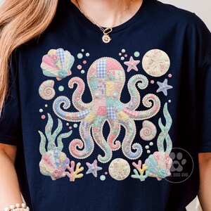 May include: A dark navy blue t-shirt featuring a central graphic of an octopus with a patchwork pattern in pastel colours. The design includes surrounding sea elements like seashells, starfish, coral, and bubbles, all rendered in a soft, quilted aesthetic.