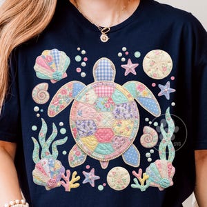 May include: A navy blue t-shirt featuring a central sea turtle graphic composed of pastel-colored patchwork patterns. The design includes surrounding elements like seashells, starfish, sand dollars, and seaweed in soft floral and gingham prints.