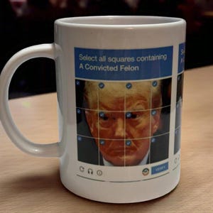 May include: White ceramic mug with a graphic of a man's face on a grid with check marks. The text on the mug reads "Select all squares containing A Convicted Felon".