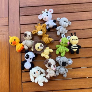 May include: A collection of 12 crocheted animal plushies in various colors, including a cow, monkey, giraffe, lion, panda, dog, koala, frog, bee, duck, and bunny.