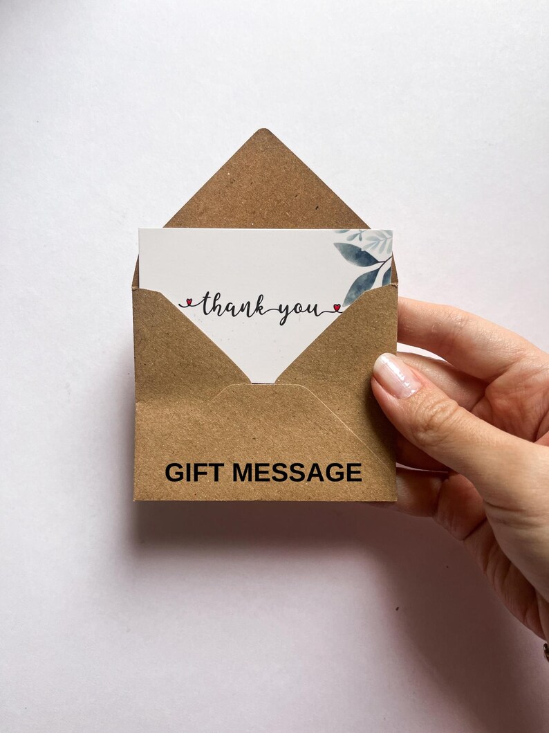 Op de afbeelding: Een bruine kraftpapieren cadeauboodschappenkaart met een witte kaart erin. De witte kaart heeft de woorden "thank you" in een scriptlettertype met een klein hartje aan het einde van elk woord. De cadeauboodschappenkaart heeft de woorden "GIFT MESSAGE".