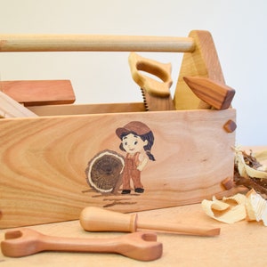 May include: A wooden toy toolbox with a handle, a saw, a hammer, a screwdriver, a wrench, and a ruler. The toolbox is decorated with a cartoon image of a girl holding a log.