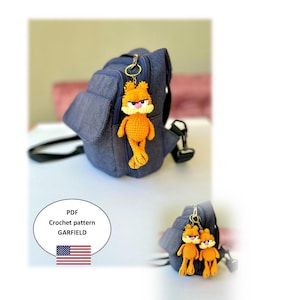 Puede incluir: Un llavero de Garfield naranja hecho a mano con ganchillo, sujeto a una mochila vaquera azul. El llavero presenta un diseño detallado del gato de dibujos animados. Una segunda imagen muestra dos llaveros de Garfield. La imagen también incluye el texto: "PDF Crochet pattern GARFIELD".