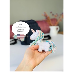 May include: PDF crochet pattern for a white unicorn keychain with a rainbow mane and tail. The pattern is available for download.