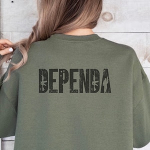 Op de afbeelding: Een militair groen sweatshirt met het woord "DEPENDA" in zwart gedrukt op de achterkant met een verweerde look. Het woord wordt geflankeerd door twee gestileerde geweren en een silhouet van een soldaat.