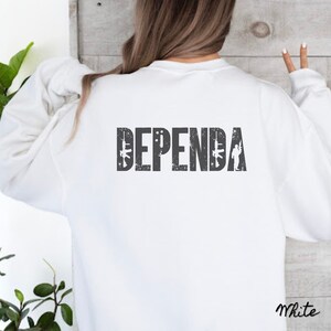 May include: White sweatshirt with the text "DEPENDA" printed in gray on the back. The text is stylized with a distressed look and includes small graphic images of rifles and a soldier.