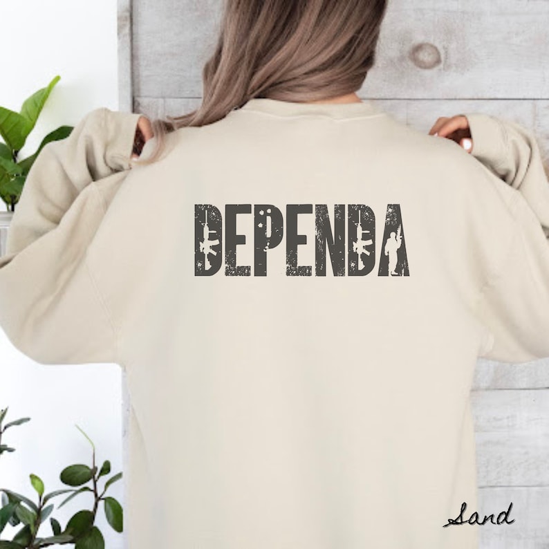 May include: A beige sweatshirt with the word "DEPENDA" printed on the back in black with a distressed look. The word is surrounded by small images of guns and soldiers.