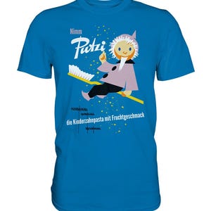 Op de afbeelding: Een helderblauwe t-shirt met een cartoonillustratie van een personage op een tandenborstel. Het personage draagt een roze jas en een witte hoed. De tekst op de shirt luidt "Nimm Putzi" en "die Kinderzahnpasta mit Fruchtgeschmack".