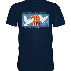 Könnte beinhalten: Ein marineblaues T-Shirt mit einer Vintage-Grafik von zwei weißen Tauben, die einen roten Globus halten, mit dem Text "SONDERPOSTWERTZEICHENHEFT 1.-M DEUTSCHE POST DDR" und "FRIEDEN" unter dem Globus.