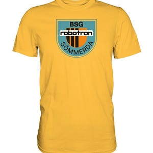 Könnte beinhalten: Gelbes T-Shirt mit einem blauen und orangenen Logo, auf dem "BSG robotron SÖMMERDA" steht.