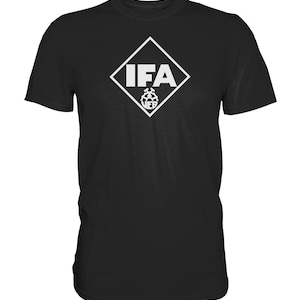 Könnte beinhalten: Schwarzes T-Shirt mit einem weißen rautenförmigen Logo, in dem "IFA" steht. Das Logo enthält auch einen kleineren weißen Kreis mit einem Zahnrad im Inneren.