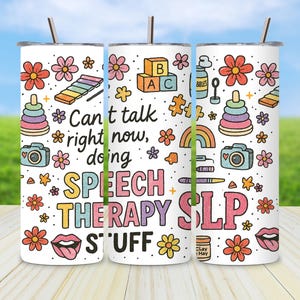 Puede incluir: Un vaso blanco con pajita, decorado con ilustraciones coloridas y el texto "Can't talk right now, doing SPEECH THERAPY SLP STUFF." El diseño incluye flores, juguetes e iconos relacionados con la terapia del habla.