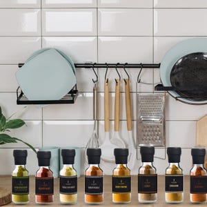 May include: A kitchen setting with a collection of spice jars, each with a black lid and label. The jars are filled with different spices, including curry powder and cumin. Kitchen utensils and plates are also visible, suggesting a cooking theme.
