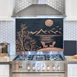 May include: A stainless steel range hood with a black and copper backsplash featuring a mountain scene with a full moon. The backsplash has a 3D embossed design.
