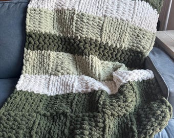 Könnte beinhalten: Eine dicke Strickdecke mit einem gestreiften Muster in Grün- und Weißtönen. Die Decke ist gefaltet und über ein Sofa gelegt.