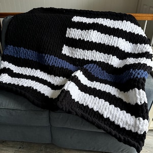 May include: A black and white striped knitted blanket with a blue stripe across the middle. The blanket is folded and draped over a couch.