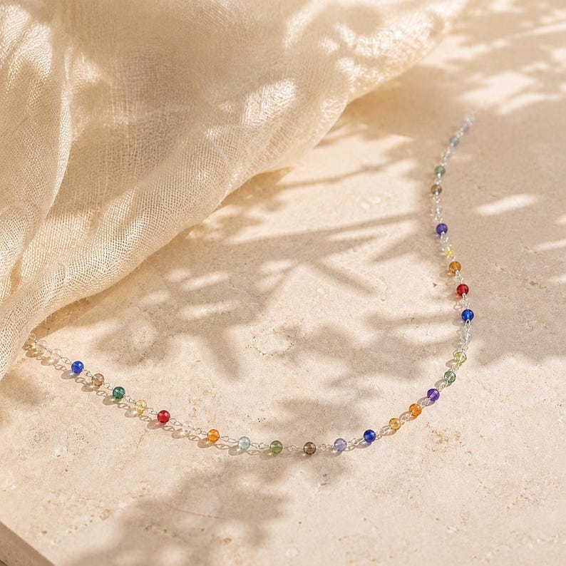 May include: A delicate necklace featuring a thin silver-toned chain interspersed with small, round, multi-colored beads in shades of red, orange, yellow, green, blue, and purple, arranged in a repeating pattern along the length of the jewelry piece.