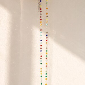 May include: A delicate necklace featuring a thin silver-toned chain interspersed with small, multi-colored faceted beads in shades of red, blue, green, yellow, and clear. The necklace includes an adjustable extender chain with a lobster clasp.