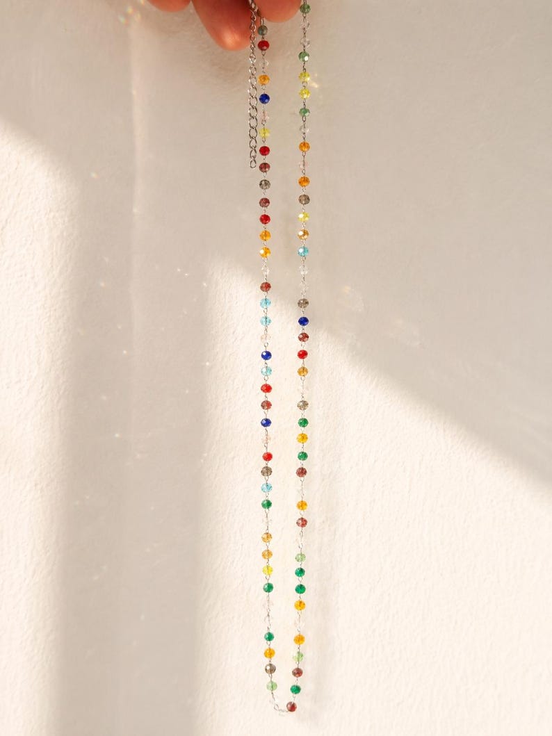 May include: A delicate necklace featuring a thin silver-toned chain interspersed with small, multi-colored faceted beads in shades of red, blue, green, yellow, and clear. The necklace includes an adjustable extender chain with a lobster clasp.