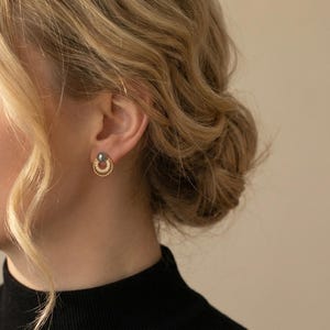 May include: A gold stud earring featuring a dark grey spherical bead at the top, connected to a small, textured gold hoop that is embellished with a series of tiny, clear, sparkling stones along its lower circular edge.