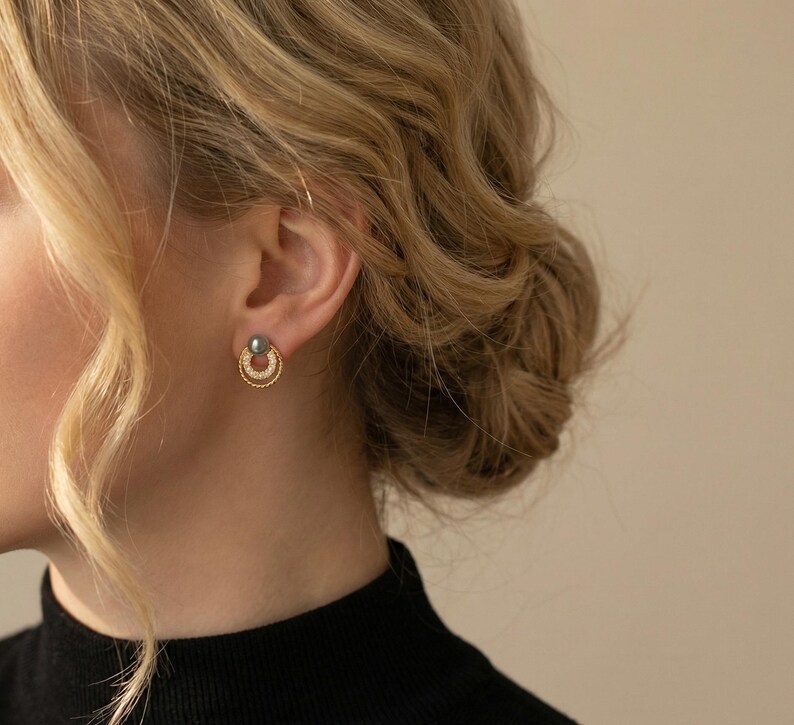 May include: A gold stud earring featuring a dark grey spherical bead at the top, connected to a small, textured gold hoop that is embellished with a series of tiny, clear, sparkling stones along its lower circular edge.
