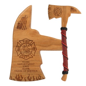 May include: A wooden firefighter axe and display stand. The axe has a red and black wrapped handle. The stand is shaped like an axe head and features the words "Fire Dept." and space for personalization. The axe and stand are made of light brown wood.