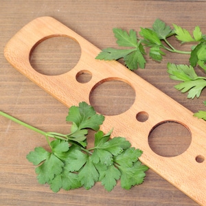 May include: A wooden tool with five circular cutouts of varying sizes. The tool is designed for cutting herbs and vegetables into uniform shapes. The tool is lying on a wooden surface with fresh parsley leaves scattered around it.