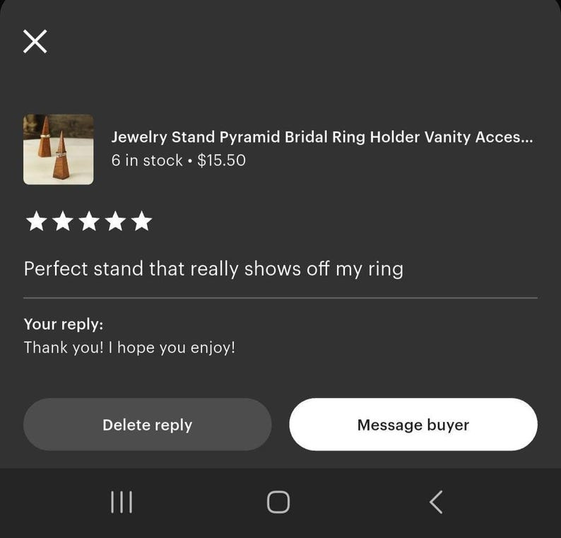 May include: A close-up of three small, pyramid-shaped jewelry stands made of a dark wood. The stands are designed to hold rings. The image is from an Etsy listing, with a customer review and seller's reply.